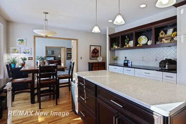 kitchen with dark brown cabinetry, dark stone countertops, pendant lighting, light hardwood / wood-style floors, and decorative backsplash