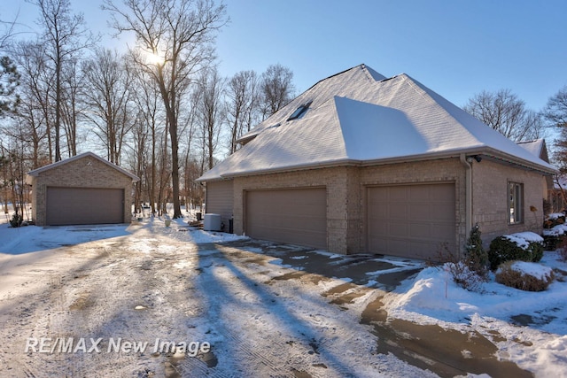 snow covered property featuring a garage, an outdoor structure, and cooling unit