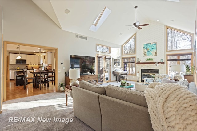 living room featuring a skylight, high vaulted ceiling, ceiling fan, and light wood-type flooring