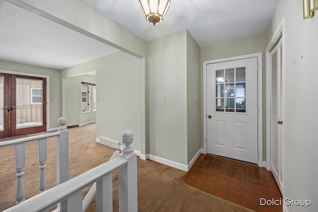 foyer featuring french doors, carpet, and a textured ceiling