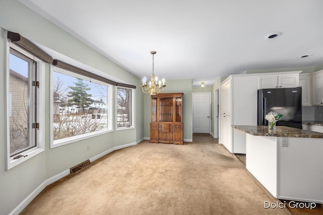 kitchen with white cabinetry, hanging light fixtures, light carpet, black refrigerator, and a notable chandelier