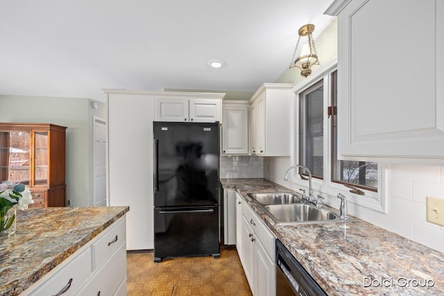 kitchen with sink, white cabinetry, light stone counters, black refrigerator, and backsplash