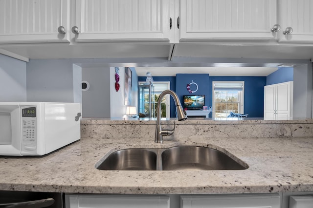 kitchen with light stone counters, sink, and white cabinets