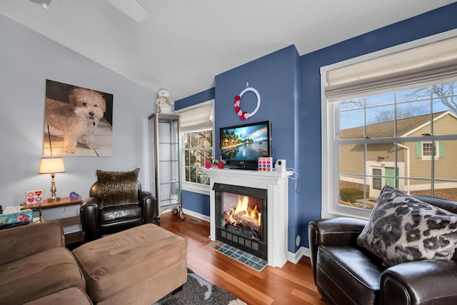 living room with a tiled fireplace, wood-type flooring, lofted ceiling, and a healthy amount of sunlight