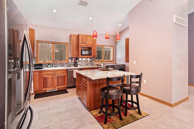 kitchen featuring a breakfast bar area, decorative light fixtures, a kitchen island, stainless steel appliances, and light stone countertops