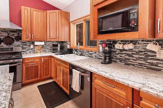 kitchen with light stone counters, black appliances, sink, and wall chimney range hood