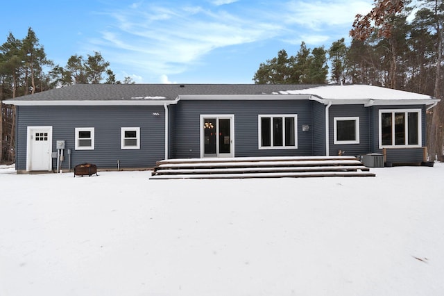 snow covered rear of property featuring central AC