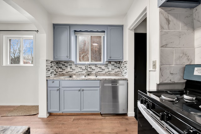 kitchen featuring black gas range oven, sink, light hardwood / wood-style flooring, backsplash, and stainless steel dishwasher