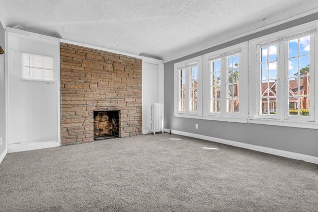 unfurnished living room featuring radiator, a wealth of natural light, carpet floors, and a large fireplace