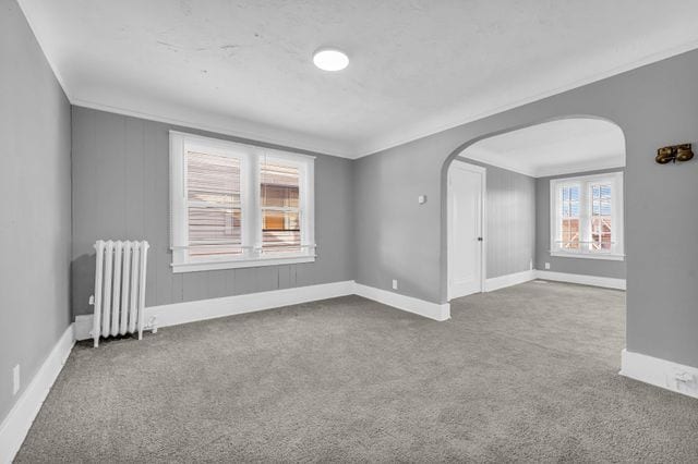 empty room featuring ornamental molding, carpet, and radiator heating unit