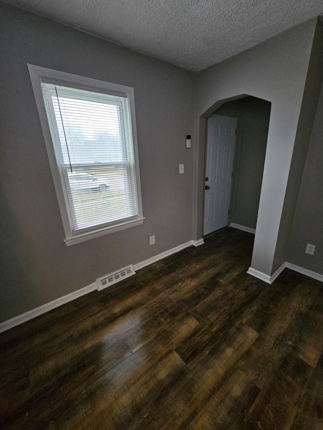 empty room with a textured ceiling and dark hardwood / wood-style flooring