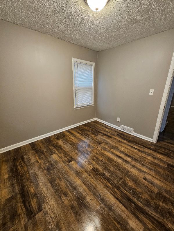 unfurnished room with dark wood-type flooring and a textured ceiling