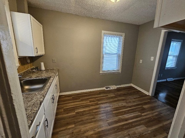 kitchen featuring sink, dark wood-type flooring, dark stone countertops, a textured ceiling, and white cabinets