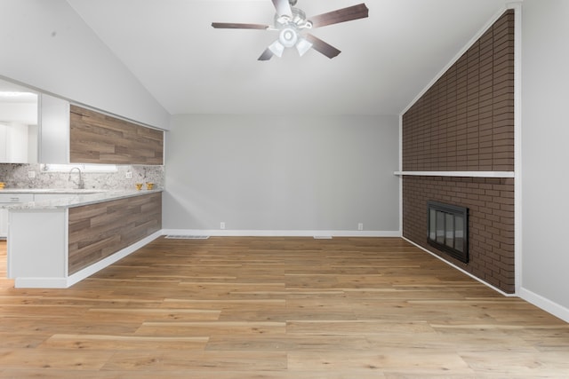 unfurnished living room featuring sink, vaulted ceiling, ceiling fan, a fireplace, and light hardwood / wood-style floors