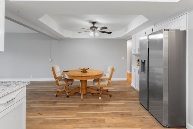 dining area with ceiling fan, light wood-type flooring, and a tray ceiling