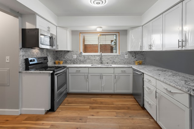 kitchen with stainless steel appliances, sink, white cabinets, and light wood-type flooring