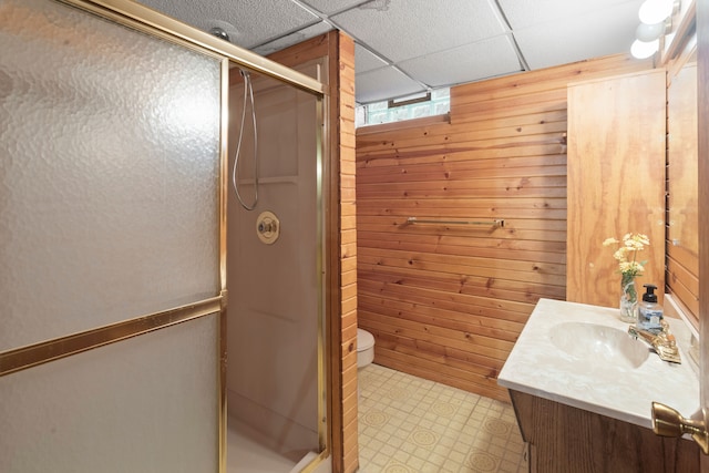 bathroom with vanity, a shower with door, a drop ceiling, and wood walls