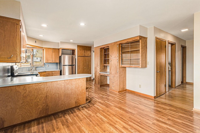 kitchen with sink, light hardwood / wood-style floors, kitchen peninsula, stainless steel appliances, and wall chimney range hood