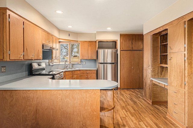 kitchen featuring a kitchen bar, sink, light hardwood / wood-style flooring, kitchen peninsula, and stainless steel appliances