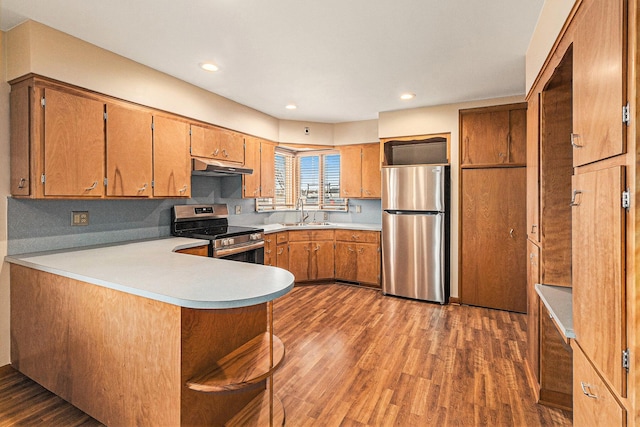 kitchen featuring stainless steel appliances, dark hardwood / wood-style flooring, kitchen peninsula, and sink