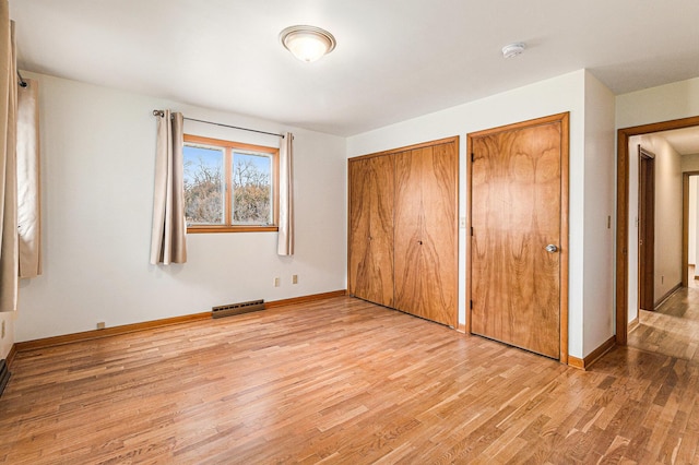 unfurnished bedroom with light hardwood / wood-style floors and two closets