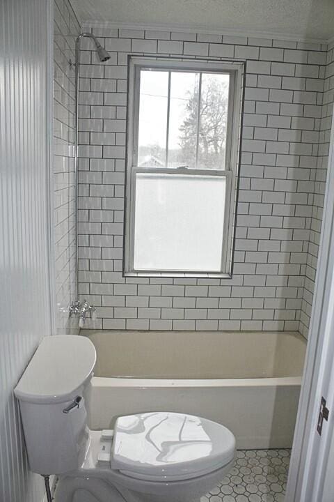 bathroom featuring tiled shower / bath combo, tile patterned floors, a textured ceiling, and toilet