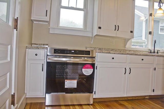 307 New York Ave, Dowagiac, MI 49047 - kitchen with white cabinetry, oven, wood finished floors, and light stone counters