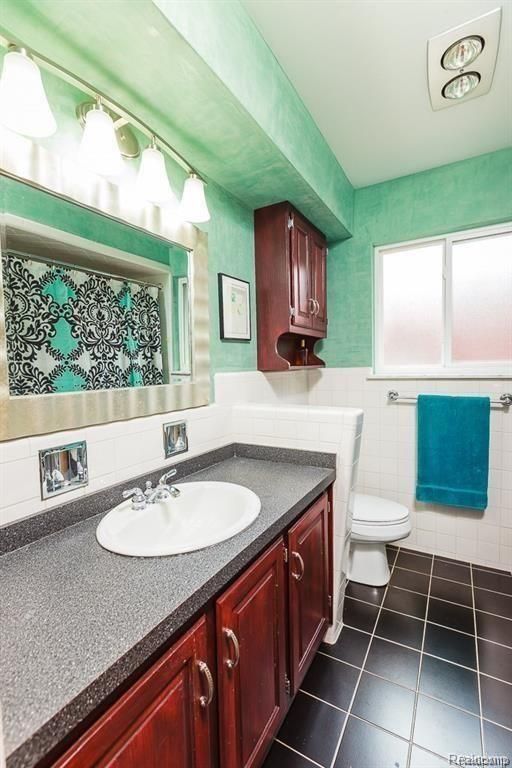 bathroom featuring vanity, tile patterned floors, tile walls, and toilet