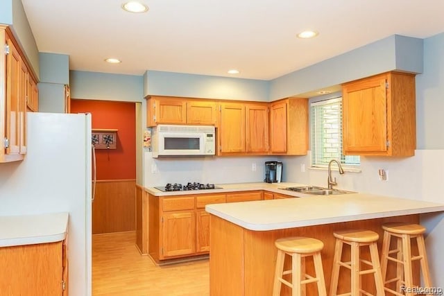 kitchen featuring sink, white appliances, light hardwood / wood-style flooring, a kitchen breakfast bar, and kitchen peninsula