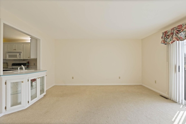 unfurnished living room featuring a sink, baseboards, light carpet, and visible vents