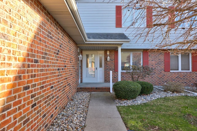 view of exterior entry featuring brick siding and a shingled roof