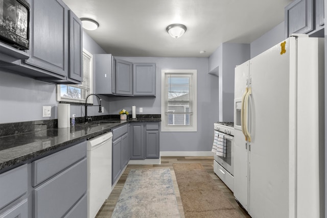 kitchen featuring sink, gray cabinets, hardwood / wood-style flooring, white appliances, and dark stone counters