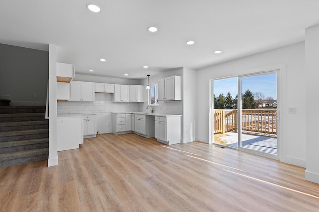 kitchen featuring sink, light wood-type flooring, stainless steel dishwasher, pendant lighting, and white cabinets