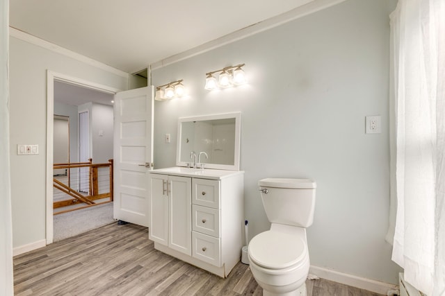 bathroom with hardwood / wood-style flooring, crown molding, a baseboard heating unit, vanity, and toilet