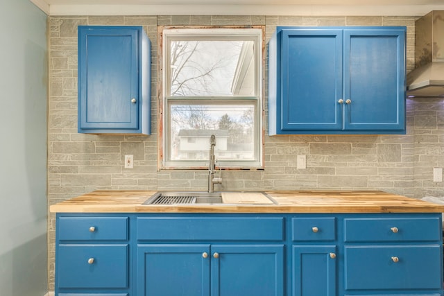 kitchen featuring blue cabinets, sink, decorative backsplash, and wall chimney range hood