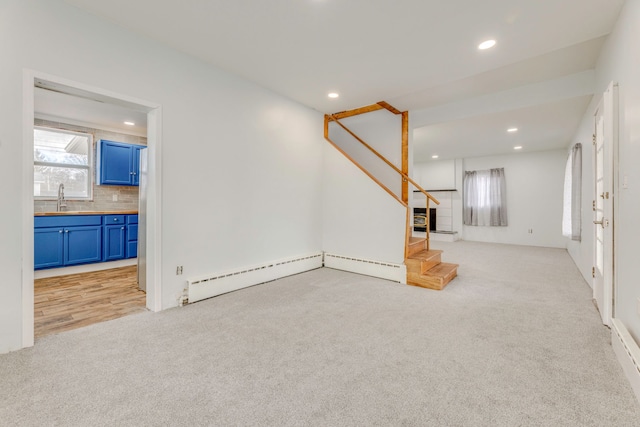 unfurnished living room with sink, light carpet, and baseboard heating