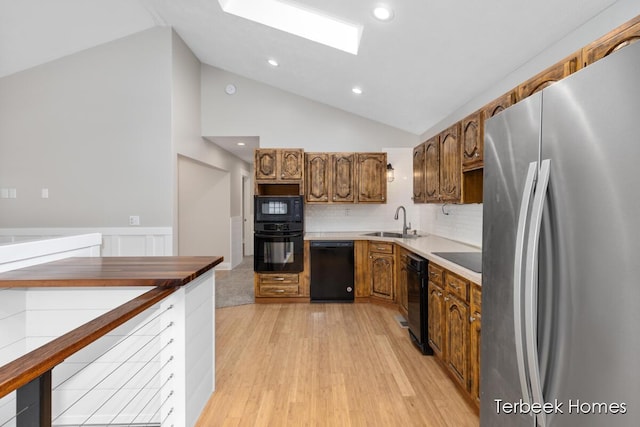 kitchen featuring sink, light hardwood / wood-style flooring, a skylight, black appliances, and decorative backsplash