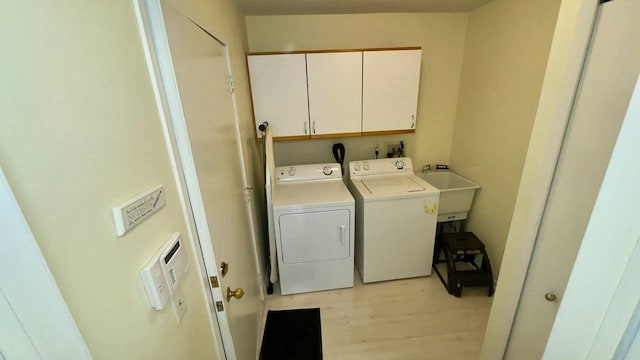 washroom with independent washer and dryer, sink, light hardwood / wood-style floors, and cabinets