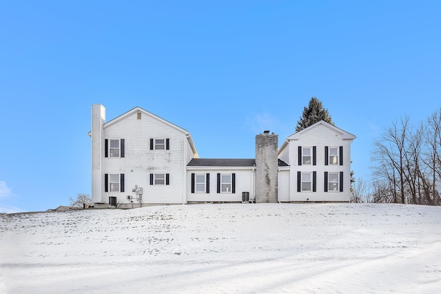 snow covered back of property featuring central AC and a chimney