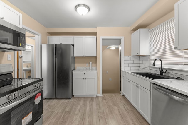 kitchen with appliances with stainless steel finishes, white cabinetry, sink, light stone counters, and light wood-type flooring