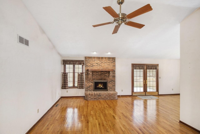 unfurnished living room featuring french doors, vaulted ceiling, a brick fireplace, light hardwood / wood-style flooring, and ceiling fan