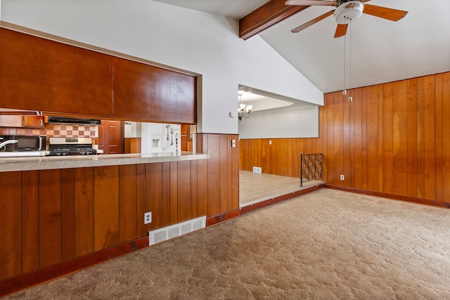 kitchen with wood walls, vaulted ceiling with beams, light carpet, stainless steel stove, and exhaust hood