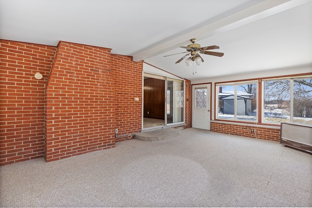 unfurnished living room with lofted ceiling with beams, ceiling fan, brick wall, and carpet floors