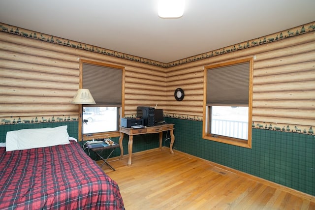 bedroom featuring hardwood / wood-style flooring, rustic walls, and multiple windows