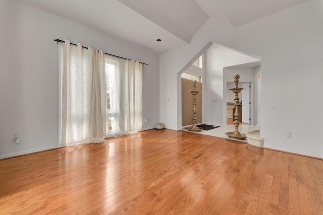 unfurnished living room with light wood-style flooring, arched walkways, and baseboards