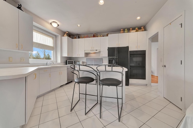 kitchen with under cabinet range hood, a kitchen bar, black appliances, and light tile patterned floors