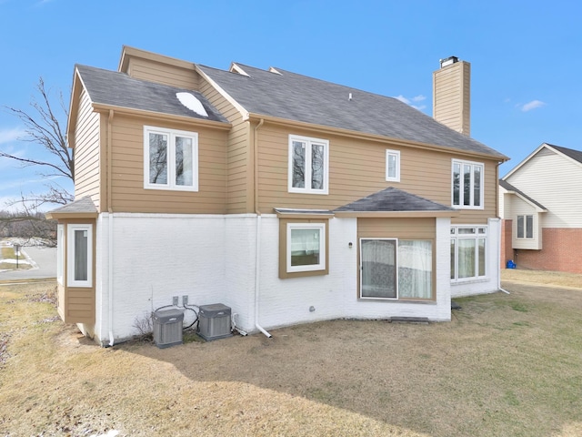 back of property featuring brick siding, central air condition unit, a lawn, and a chimney