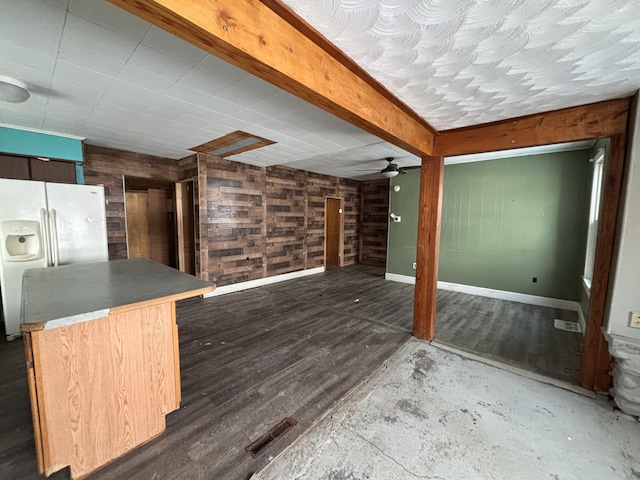 interior space featuring dark wood-type flooring, ceiling fan, wooden walls, and white fridge with ice dispenser