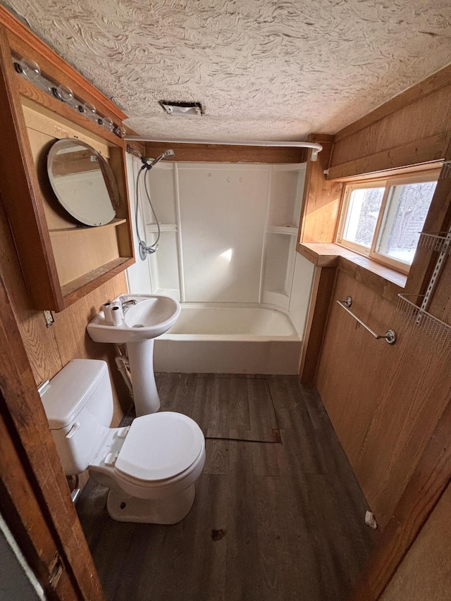 bathroom featuring wood walls, wood-type flooring, toilet, bathing tub / shower combination, and a textured ceiling