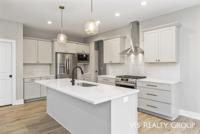 kitchen featuring stainless steel appliances, hanging light fixtures, a sink, wall chimney range hood, and an island with sink
